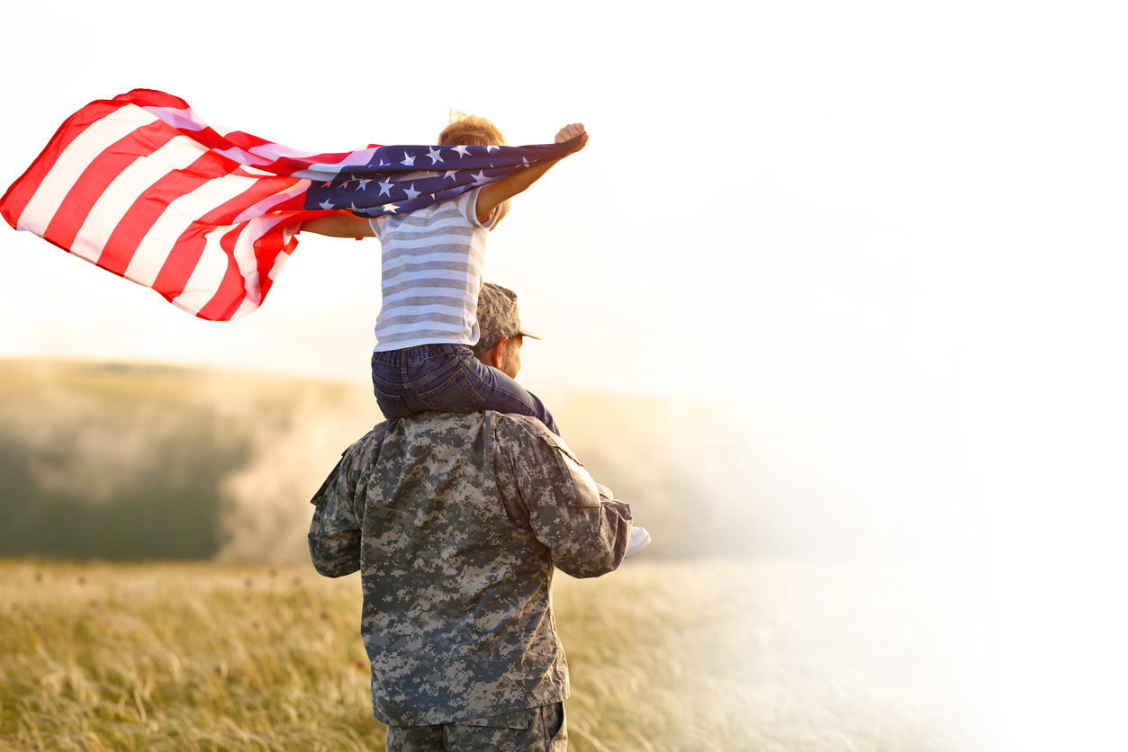 veteran with child on shoulders, holding a flag