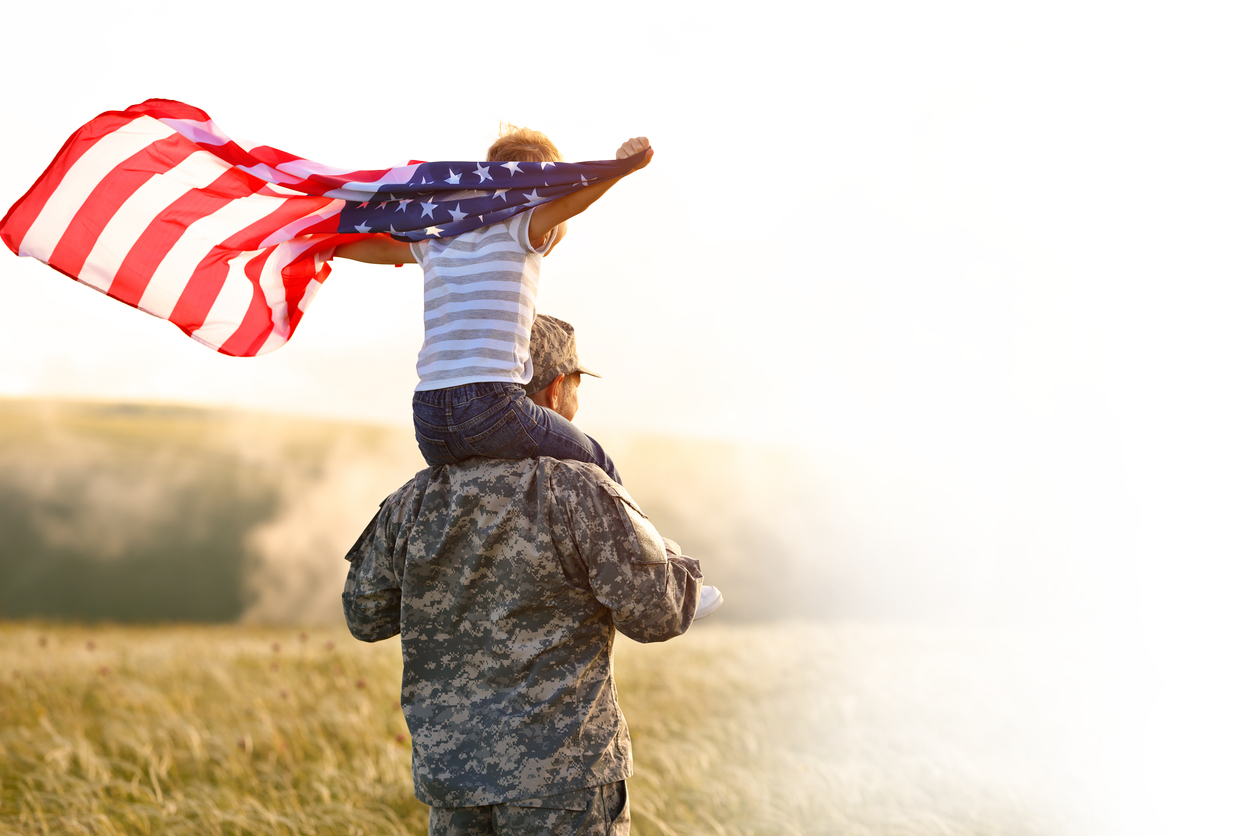 veteran with child on shoulders, holding a flag